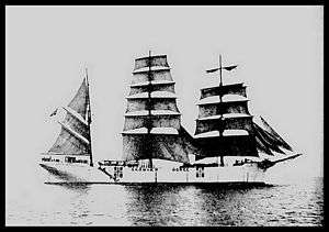 Huge ship with many sails, most of which are down, carrying Norwegian flags and reading "Skomvær Norge"