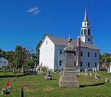 A white church, seen from the side slightly to its rear, with a cemetery in front