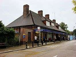 A brown-bricked building with four brown-bricked chimneys and a rectangular, dark blue sign reading "STANMORE STATION" in white letters