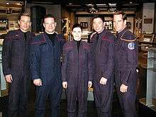 Five people in blue jumpsuits stand in a row.