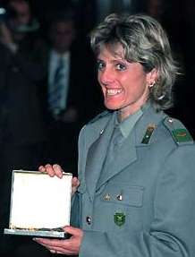 A smiling woman, wearing a green suit, holds an award.