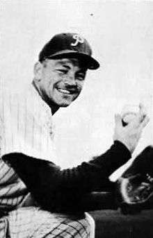 A black and white image of a smiling man in a baseball uniform holding a baseball