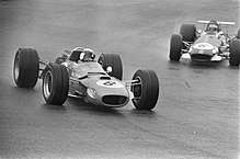 Black-and-white photograph of two Formula One cars driving on a wet track