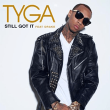 The cover consists of a white background that has the artist's name on the top left corner, boldly written in gold. Below it is the song title and featured artist's name, both colored in black and light gold respectively. The artist is centered on the cover, leaning his head towards his left, wearing a white shirt and black leather jacket covered in gold studs, sunglasses, and a gold watch and bracelet on his wrists.