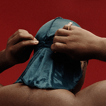 A man adjusting his durag on a red background.