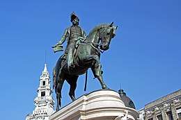 Photograph of a bronze statue with a man on horseback wearing a bicorn hat and military dress and who holds forth a scrolled sheaf of paper