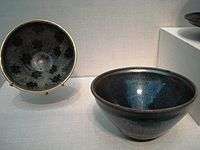 Two small polished black bowls. One has a large blue streak in it, the other has a polka-dot pattern on the inside consisting of black spots on a dark grey background. All of the coloring is created by features of the stone, rather than paint.