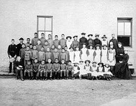 Posed, group photo of students and teachers, dressed in black and white, outside Middlechurch, Manitoba's St. Paul's Indian Industrial School