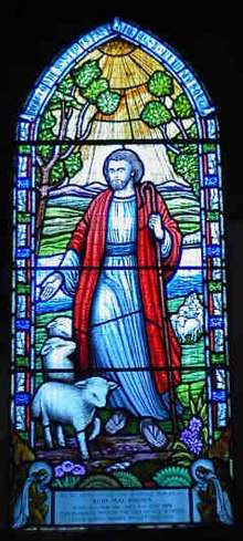Gothic-arched stained glass window, depicting a shepherd with his flock.