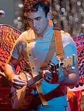 A young Caucasian man with short, dark hair plays a banjo.