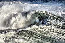 Photo showing surfer inside the curl of a breaking wave in turbulent waters