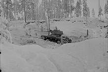A Soviet light tank, seen from its left side, is described by the Finnish photographer as advancing aggressively in the snowy forested landscape during the Battle of Kollaa.