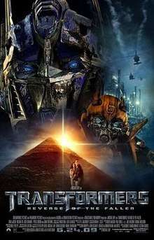 The faces of two robots stand atop a pyramid. A helicopter flies over an industrial facility on the right side of the image, and a young couple is seen in front of the pyramid. The film title and credits are on the bottom of the poster.