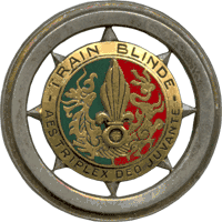 A circular insignia, divided roughly into green and red halves. The phrase "Train Blinde – Aes Triplex Deo Juvante" surrounds the coloured halves.