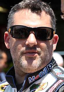 A man in his mid forties wearing sunglasses and black and white racing overalls
