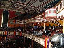 A view away from the stage shows painted front edges of two balconies and the decorated ceiling.