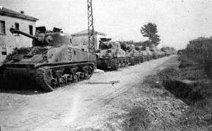 A black and white photograph of several tanks in a column along a road