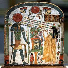 Painted wood panel showing a woman with arms upraised toward a man with a falcon's head and a sun-disk crown. Chains of flowers-like shapes radiate from the disk toward the woman's face.