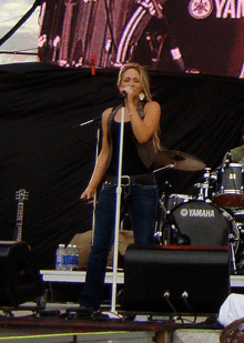 A woman sings into a microphone, her entire height shown.