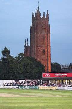 Cricket ground in front of a church tower.