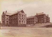 Sepia photograph of the buildings of the technical college. The unsealed Harris Street runs across the foreground and Mary-Anne street goes into the distance over a hill with the collection of buildings and their elaborate brickwork standing on the corner.