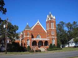 Photo of a red brick church with steeple, three arches and white painted trim.