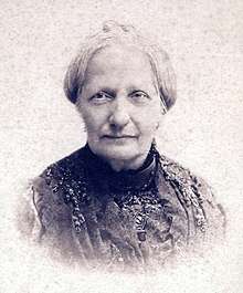 Head and shoulders sepia photograph showing an older woman with gray hair and wearing a dark lace dress