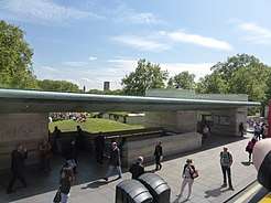 Entrance and shelter on Piccadilly, a green copper roof spans between two stone structures with a view of a park between