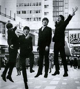 A black and white image of four suited men captured mid-jump