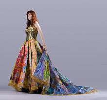 A mannequin wears a multicolored gown with a golden bodice, full skirt, and flowing train.