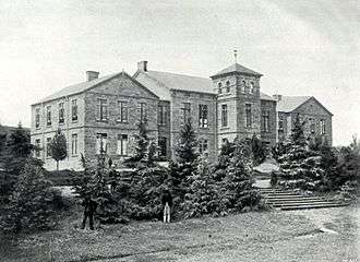 A black and white photograph of a large mansion house, surrounded by various trees