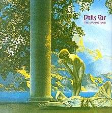 A predominately green, yellow, and blue saturated Ancient Greek-style image of a girl lying down smiling and another girl standing above her, naked, looking down at her. Next to them is a column. The leaves of a tree are visible directly behind the column. In the background is a large mountain, separated by the sea. "Dalis Car", with "The Waking Hour" below it in smaller text, are imprinted in fantasy-style purple text in the upper-right corner.