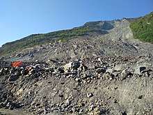 The debris of the Xinmo landslide as seen on 15 May 2018 from the reconstructed road. A red flag stands in memory of the victims.