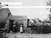 women in traditional dress at church gate with church and graveyard in background in 1885