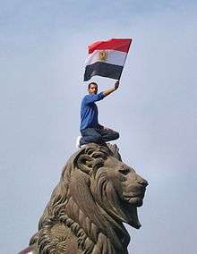 Man crouched on top of the famous Qasr al-Nil Bridge stone fish, waving the Egyptian flag