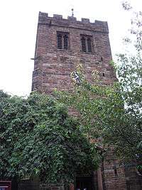 A stone tower with a doorway flanked by columns, a clock face, louvred bell openings, and a battlemented parapet