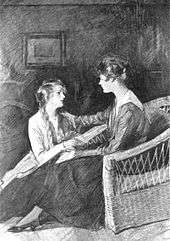  Two young women face each other, one (right) seated in a chair, the other sitting on the floor. They are lookng intently at each other; the one on the right has placed her right arm on the other's left shoulder.