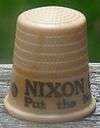 An off-white thimble, with the visible black lettering, "NIXON/Put the ne&nbsp;...