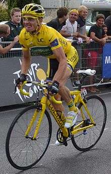A cyclist in his mid-thirties, wearing an all-yellow jersey with green and white trim, with a yellow helmet, sitting atop an all-yellow bicycle.