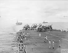 Black and white photograph with the deck of an aircraft carrier in the foreground and two other aircraft carriers in the background