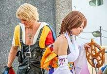 Young man and woman dressed as Tidus and Luna. Tidus wears dark leather overalls, and Luna is dressed in white.