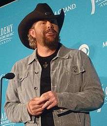 A bearded man wearing a grey shirt and a black cowboy hat