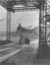 A ship slides out from under a steel framework and into the water.