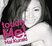 A young woman, who has her hands up and smiling. The words "touch Me!" is written pasted her body in pink.