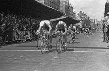 Cyclists crossing a finish line in front of spectators