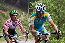 Thomas Voeckler wearing a white jersey with red polka dots, following Fredrik Kessiakoff as they ride up an incline