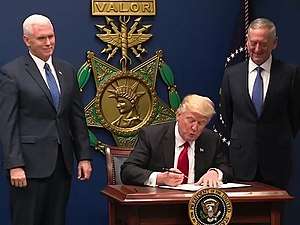 Donald Trump signing the order in front of a large replica of a USAF Medal of Honor, with Mike Pence and James Mattis at his side