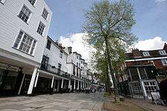 Pedestrian street paved with flagstones, lined with trees and brick and clapboard buildings, under a partly clouded sky