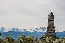 The tower of a church and snowy mountains in the distance