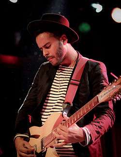 A picture of George "Twin Shadow" Lewis Jr., a man in his late 20s. He plays the guitar.